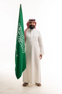 رجل سعودي بالزي التقليدي مع العلم الوطني