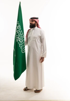 رجل سعودي يحمل العلم الوطني بالثوب التقليدي