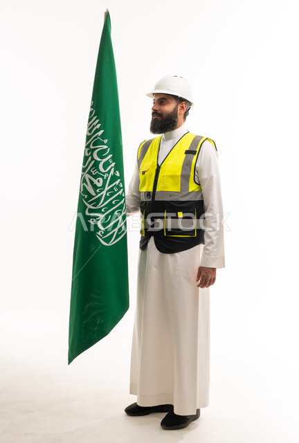 مهندس سعودي بالثوب والزي الواقي يحمل علم السعودية