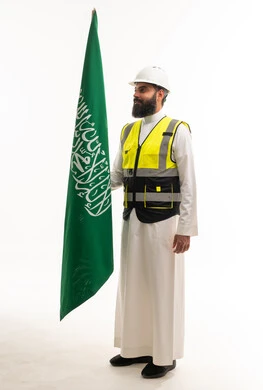 مهندس سعودي بالثوب والزي الواقي يحمل علم السعودية