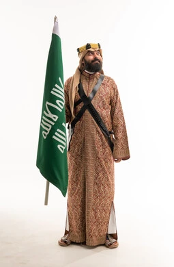 رجل سعودي بالزي الشعبي التقليدي يحمل العلم