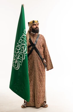 رجل سعودي بالزي الشعبي التقليدي يحمل علم السعودية