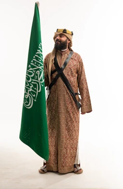 رجل سعودي بالزي التراثي يحمل علم المملكة العربية السعودية