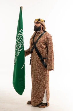 رجل سعودي بالزي التقليدي يحمل العلم الوطني
