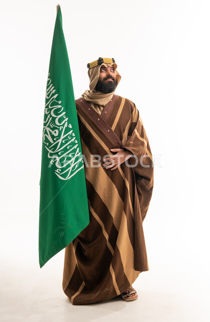 رجل سعودي بالفروة الشتوية التقليدية يحمل العلم الوطني
