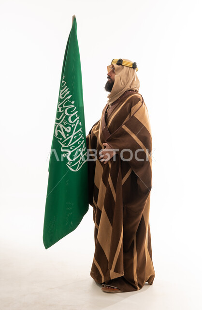 رجل سعودي بالبشت التقليدي يحمل علم المملكة العربية السعودية