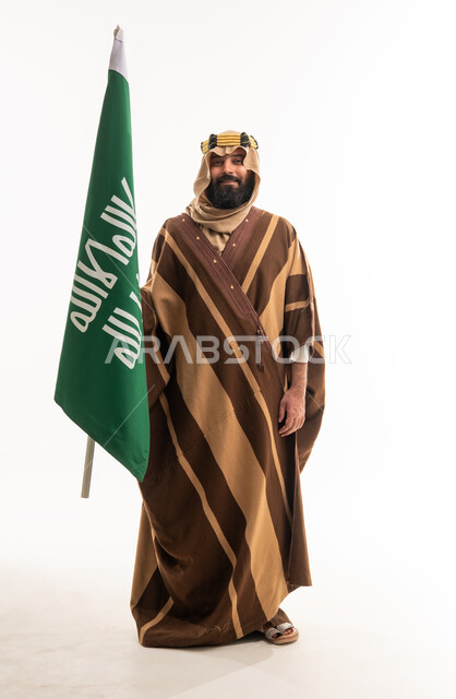 رجل سعودي بالبشت التقليدي يحمل العلم الوطني