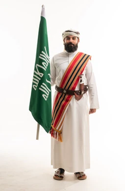 رجل سعودي بالزي النجدي التقليدي يحمل العلم