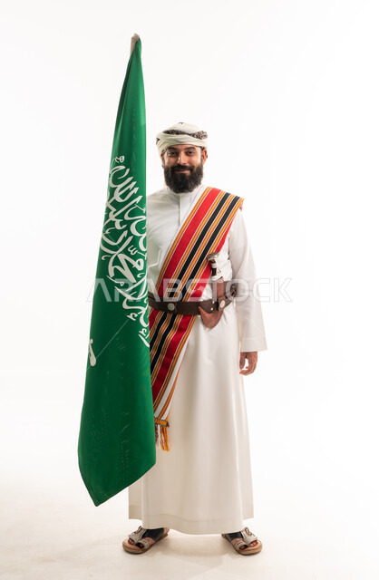 رجل سعودي بالزي التراثي الجنوبي حاملاً علم المملكة