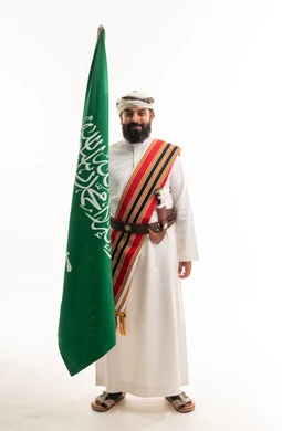 رجل سعودي بالزي التراثي الجنوبي حاملاً علم المملكة
