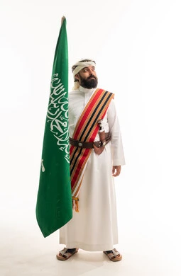 رجل سعودي بالزي النجدي التقليدي يحمل العلم