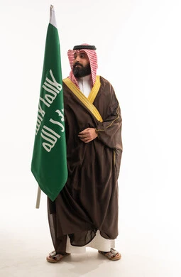 رجل سعودي بالبشت التقليدي يمسك علم المملكة