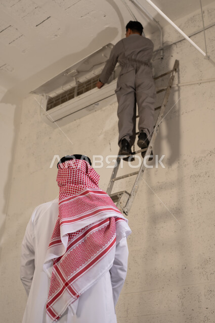 رجل سعودي يراقب فني يصلح مكيف هواء