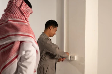 رجل سعودي يراقب فني آسيوي يصلح مقبس كهربائي