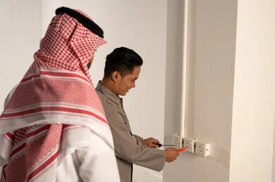 رجل سعودي يراقب فني تركيب مقابس كهربائية