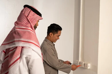 رجل سعودي يراقب فني يقوم بإصلاح المقابس الكهربائية