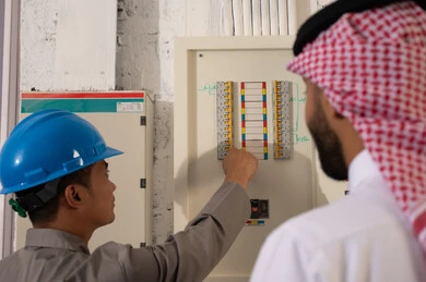 فني كهرباء يفحص لوحة مفاتيح مع رجل سعودي