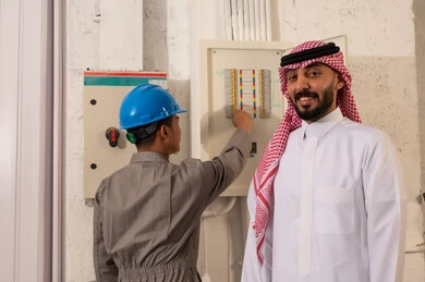 رجل سعودي وفني كهرباء يتفقدان لوحة توزيع الكهرباء