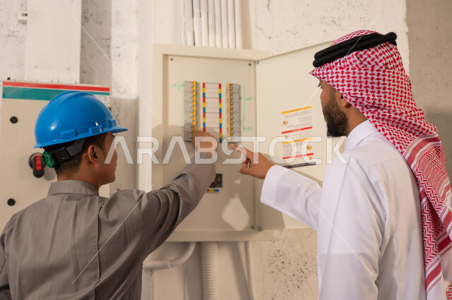 رجل سعودي وفني يفحصان لوحة الكهرباء