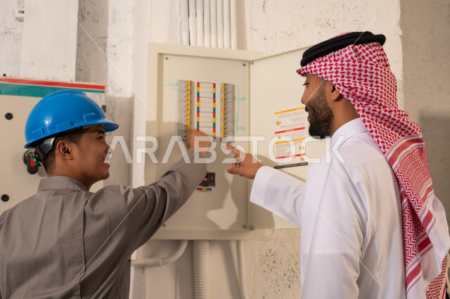 رجل سعودي وفني يتفحصان لوحة توزيع الكهرباء