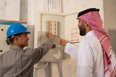 رجل سعودي وفني يتفحصان لوحة توزيع الكهرباء
