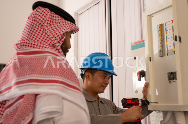 رجل سعودي وفني صيانة يصلحان لوحة كهرباء