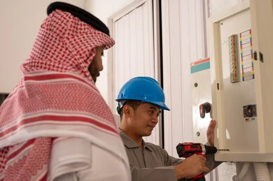 رجل سعودي وفني صيانة يصلحان لوحة كهرباء