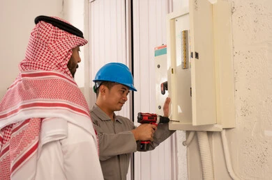 Saudi Man Supervising Asian Electrician During Repair