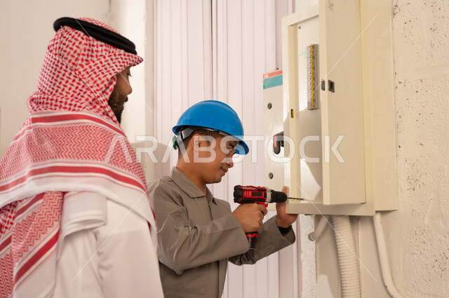 رجل سعودي يراقب فني يصلح لوحة كهرباء