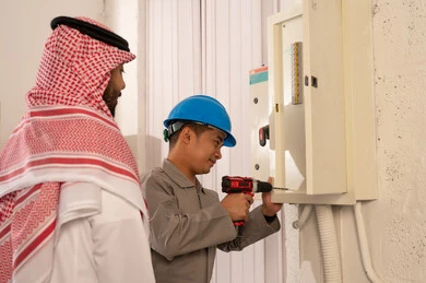 رجل سعودي يراقب فني يصلح لوحة كهرباء