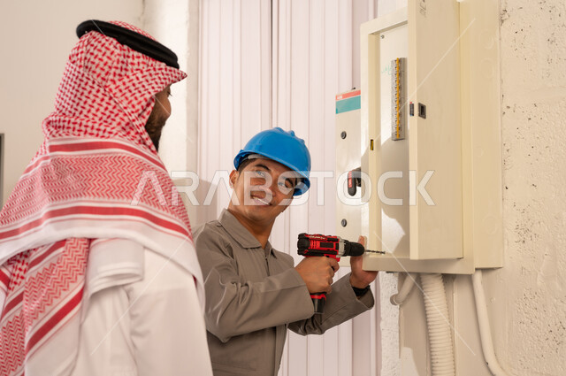 رجل سعودي يراقب فني يصلح لوحة كهربائية