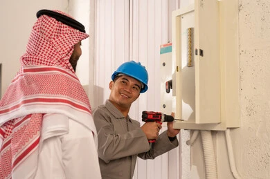 رجل سعودي يراقب فني يصلح لوحة كهربائية