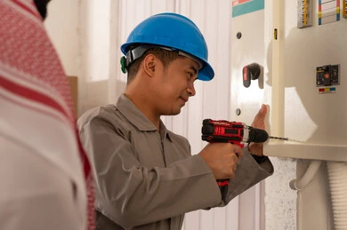 فني آسيوي يقوم بإصلاح لوحة كهرباء في السعودية