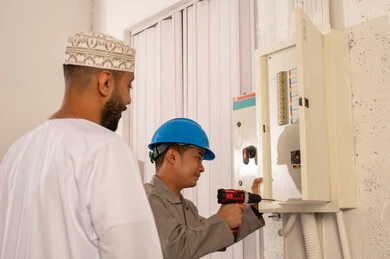 رجل عُماني يشرف على فني صيانة لوحة الكهرباء
