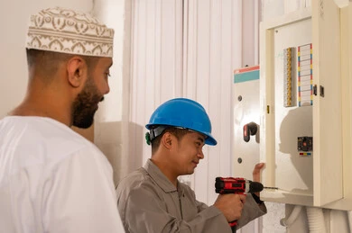 Omani Man Observing Technician Repairing Electrical Panel