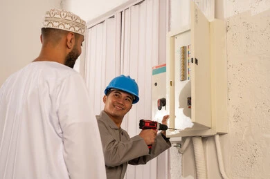 رجل عماني وعامل كهرباء فلبيني يصلحان لوحة الكهرباء