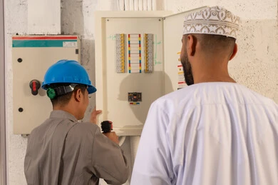 رجل عُماني وفني يفحصان لوحة مفاتيح كهربائية