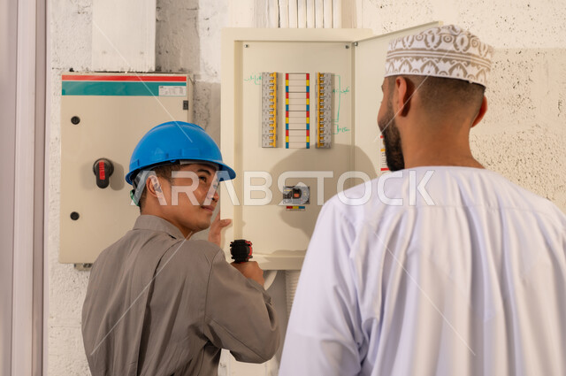 فني آسيوي ورجل عماني يفحصان لوحة توزيع الكهرباء