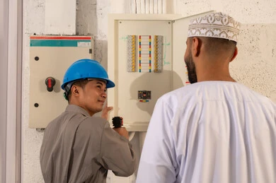 فني آسيوي ورجل عماني يفحصان لوحة توزيع الكهرباء