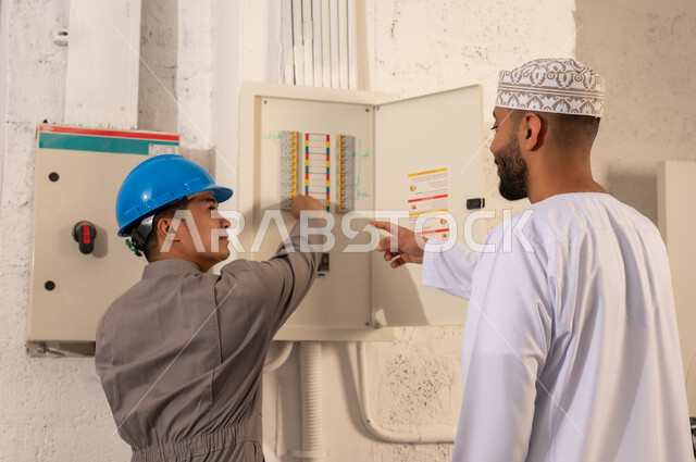 رجل عماني وفني آسيوي يفحصان لوحة مفاتيح كهربائية