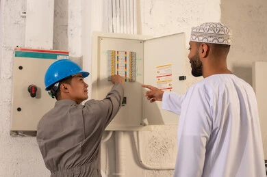 رجل عماني وفني آسيوي يفحصان لوحة مفاتيح كهربائية