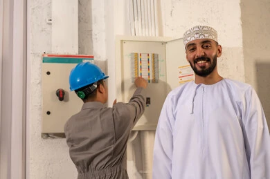 رجل عماني مع فني كهرباء يعمل على لوحة توزيع الطاقة