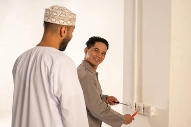 Omani Man with Electrician Repairing Wall Socket