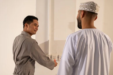 فني آسيوي مع رجل عماني يتفحصان مقابس الكهرباء