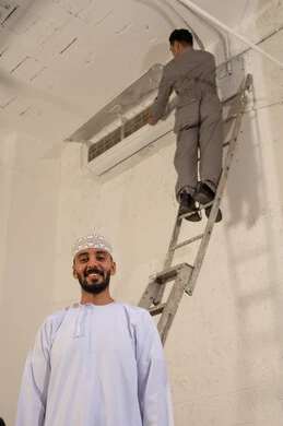 رجل عماني مع فني صيانة يقوم بإصلاح مكيف هواء