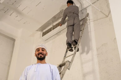 رجل عُماني وفني يقوم بإصلاح مكيف الهواء