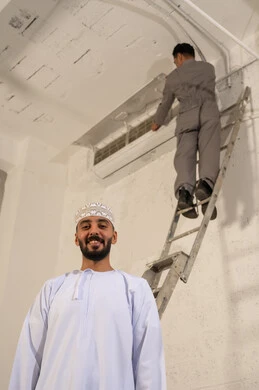 رجل عماني مع فني يقوم بإصلاح مكيف الهواء