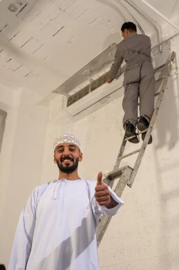 رجل عُماني وفني يقوم بصيانة وحدة تكييف الهواء