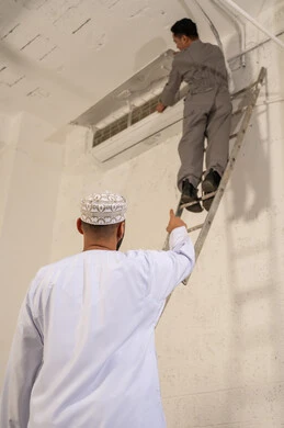 رجل عُماني وفني يقومون بإصلاح وحدة تكييف هواء