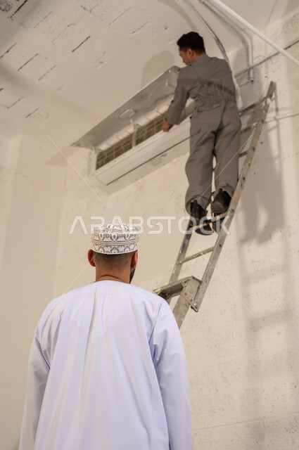 Omani Man Watching Technician Repairing Air Conditioner
